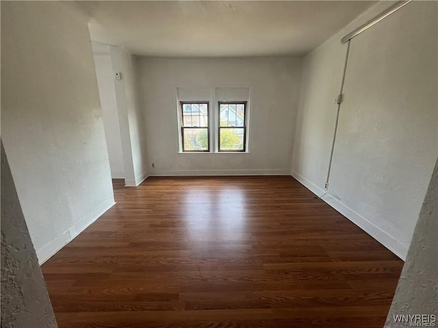 spare room featuring baseboards, dark wood-style flooring, and a textured wall