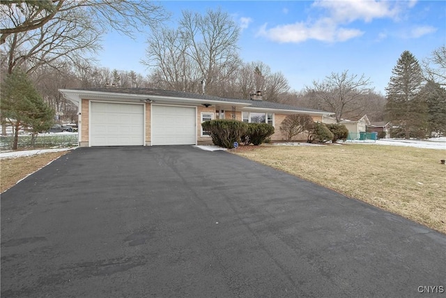 view of front of home featuring an attached garage, a chimney, a front lawn, and aphalt driveway