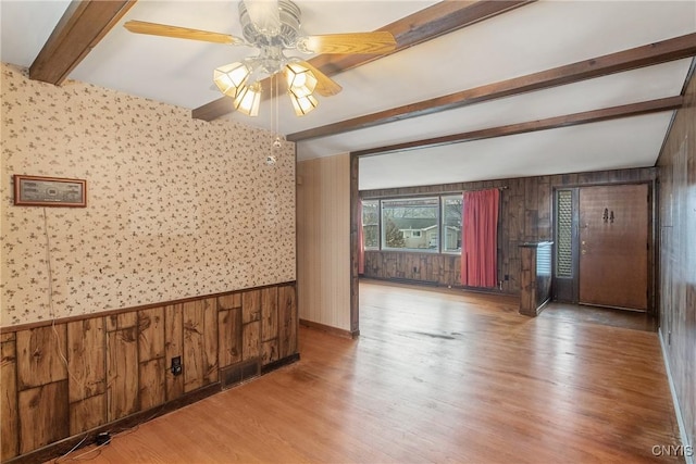 empty room with beam ceiling, light wood finished floors, visible vents, a ceiling fan, and wood walls