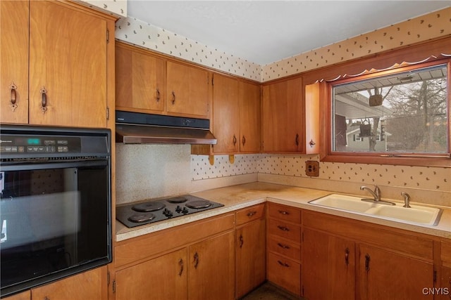 kitchen featuring wallpapered walls, under cabinet range hood, light countertops, black appliances, and a sink