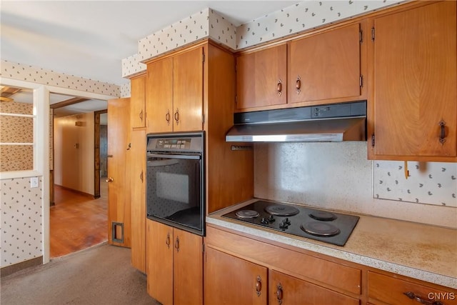 kitchen featuring black appliances, under cabinet range hood, light countertops, and brown cabinetry