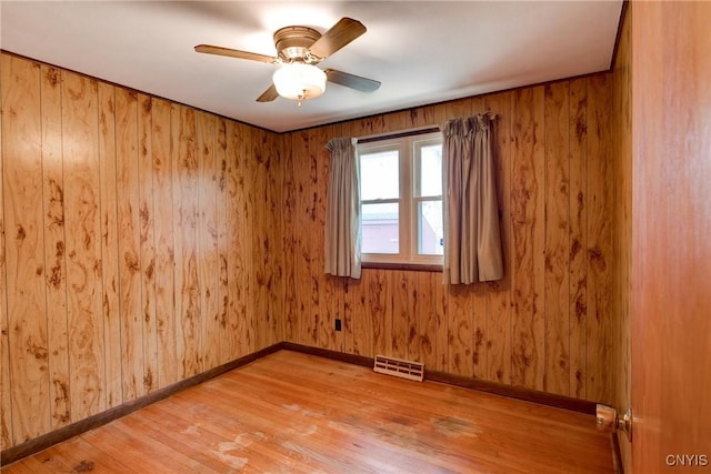 spare room featuring wooden walls, visible vents, baseboards, a ceiling fan, and light wood finished floors