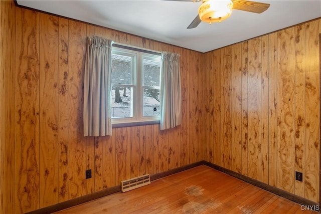 spare room with wooden walls, visible vents, baseboards, hardwood / wood-style flooring, and ceiling fan