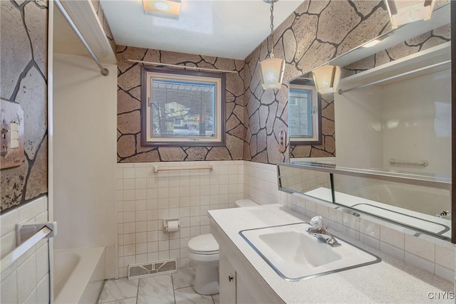 bathroom with visible vents, toilet, marble finish floor, vanity, and tile walls