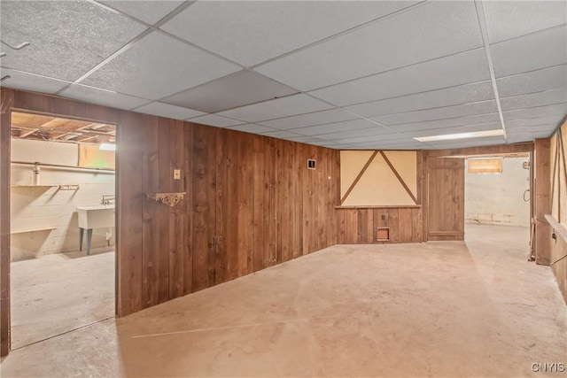 finished below grade area featuring a paneled ceiling, a sink, and wooden walls