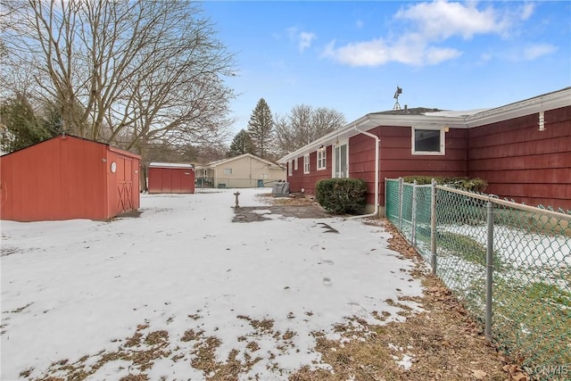 snowy yard with a storage unit, fence, and an outbuilding