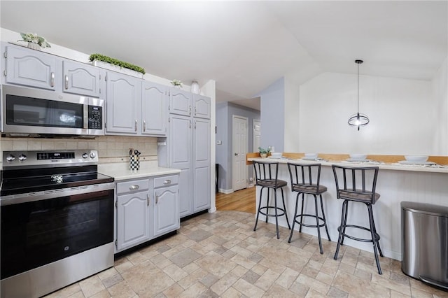 kitchen with a breakfast bar, vaulted ceiling, light countertops, appliances with stainless steel finishes, and backsplash