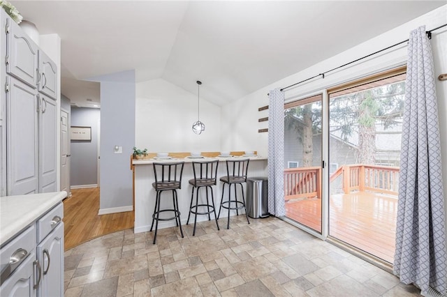 kitchen featuring decorative light fixtures, a breakfast bar area, lofted ceiling, light countertops, and stone finish floor