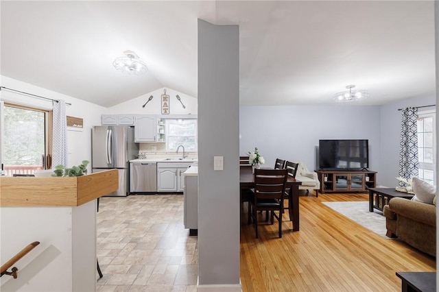 kitchen with appliances with stainless steel finishes, vaulted ceiling, light countertops, a chandelier, and a sink