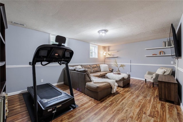 exercise area with a textured ceiling, wood finished floors, visible vents, and baseboards