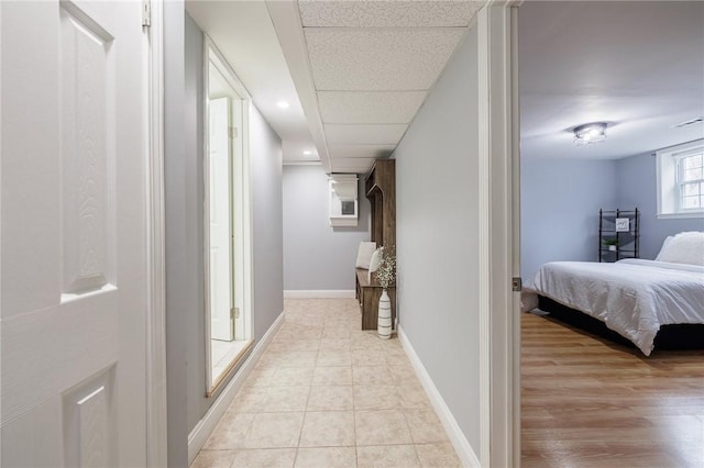 corridor with light tile patterned floors, a paneled ceiling, and baseboards