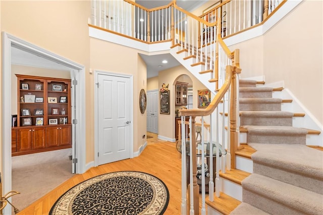 entrance foyer featuring arched walkways, wood finished floors, a towering ceiling, and baseboards