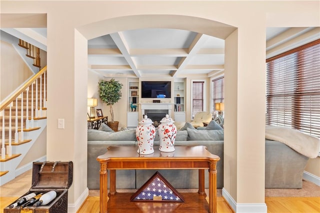 living area with baseboards, arched walkways, coffered ceiling, beamed ceiling, and built in shelves