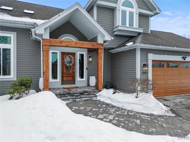 snow covered property entrance with a shingled roof and a garage