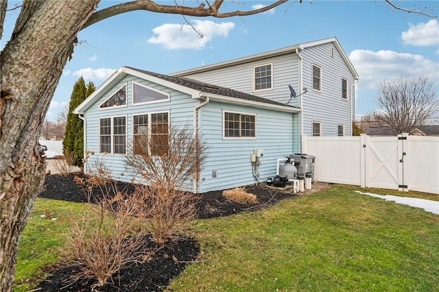 back of house with a gate, a lawn, and fence