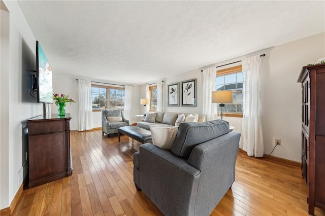 living area featuring a textured ceiling, light wood-style flooring, and baseboards