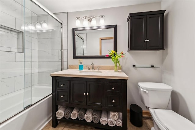 bathroom featuring toilet, combined bath / shower with glass door, and vanity