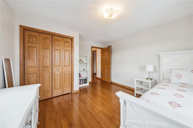 bedroom with baseboards, a textured ceiling, a closet, and light wood-style floors