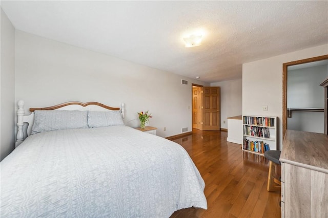 bedroom featuring visible vents, a textured ceiling, baseboards, and wood finished floors