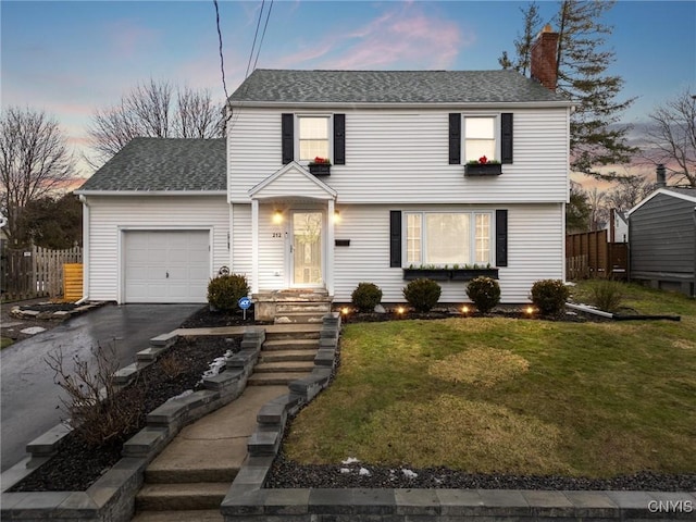 colonial inspired home with a lawn, a chimney, aphalt driveway, an attached garage, and fence