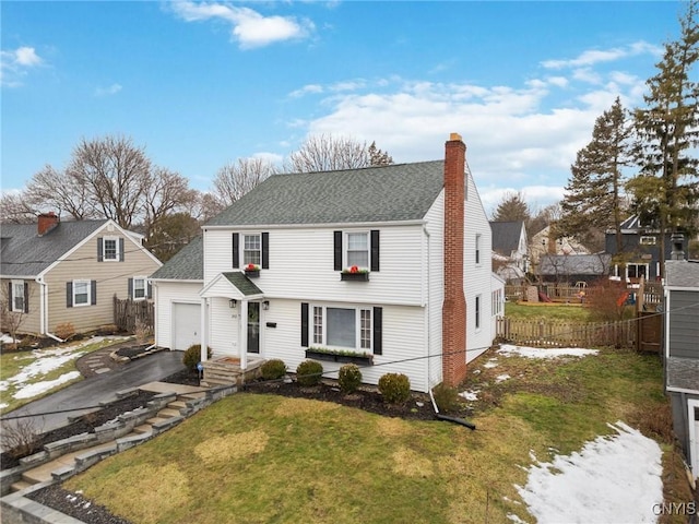 colonial house featuring an outbuilding, a chimney, a front yard, fence, and driveway