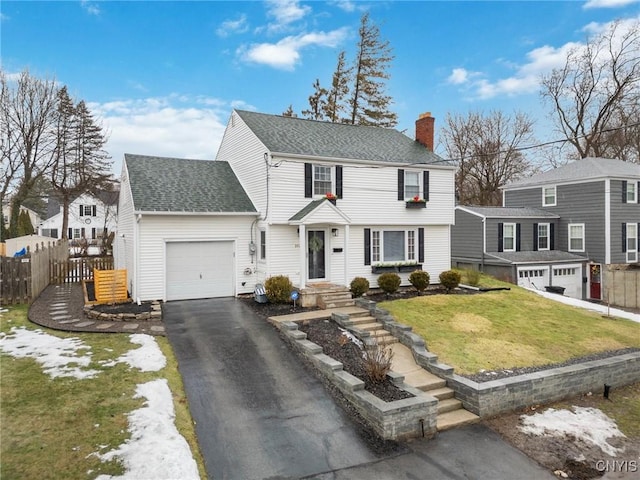 colonial house with a shingled roof, a chimney, aphalt driveway, an attached garage, and fence