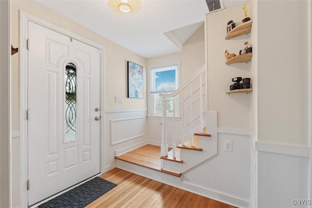 foyer entrance with visible vents, a wainscoted wall, stairway, wood finished floors, and a decorative wall