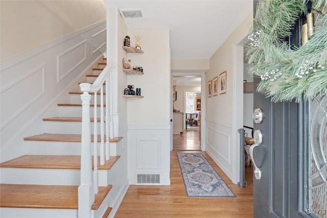 entryway with light wood-style floors, visible vents, a decorative wall, and stairway