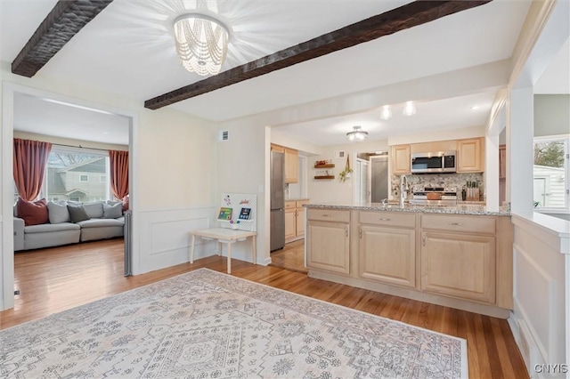 kitchen featuring light brown cabinets, appliances with stainless steel finishes, light wood-type flooring, decorative backsplash, and beamed ceiling