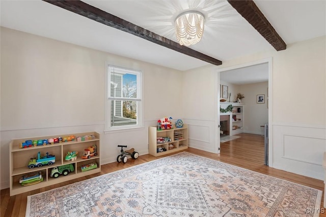 game room featuring wood finished floors, beam ceiling, and wainscoting