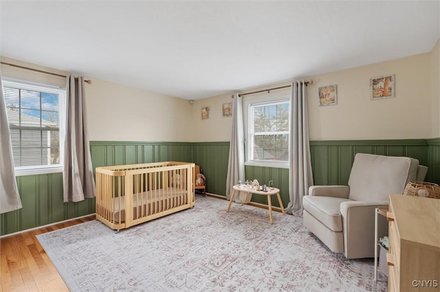 bedroom with a nursery area, wainscoting, and wood finished floors