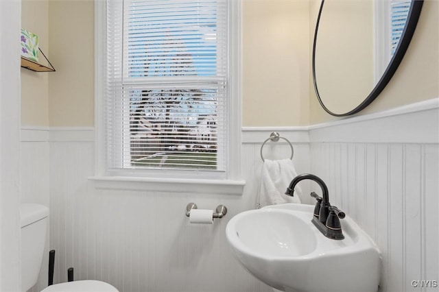 half bathroom featuring toilet, a wainscoted wall, plenty of natural light, and a sink