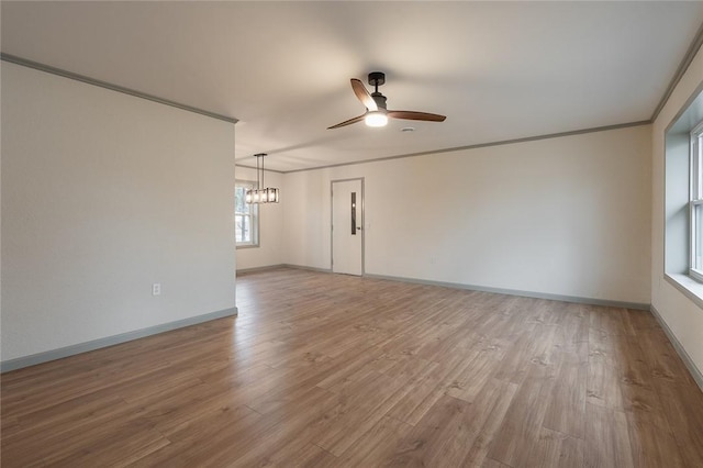 spare room with ceiling fan with notable chandelier, baseboards, wood finished floors, and crown molding