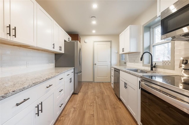 kitchen featuring light wood-style flooring, stainless steel appliances, a sink, white cabinetry, and light stone countertops