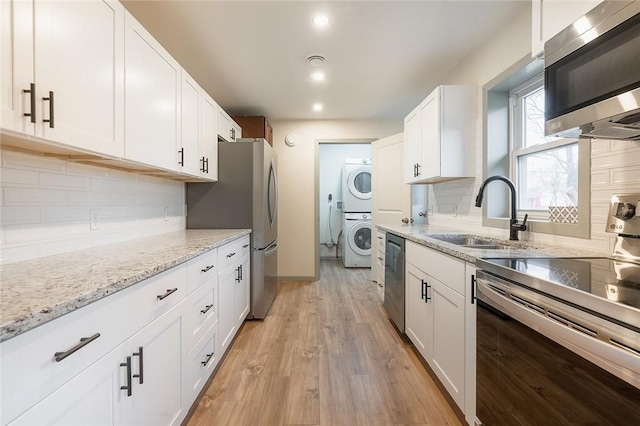 kitchen featuring a sink, white cabinets, appliances with stainless steel finishes, light wood finished floors, and stacked washer and clothes dryer