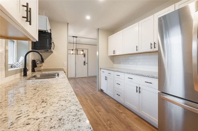 kitchen with light wood finished floors, decorative backsplash, appliances with stainless steel finishes, white cabinetry, and a sink