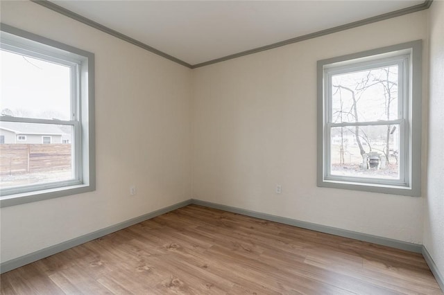 unfurnished room featuring ornamental molding, a wealth of natural light, light wood-type flooring, and baseboards