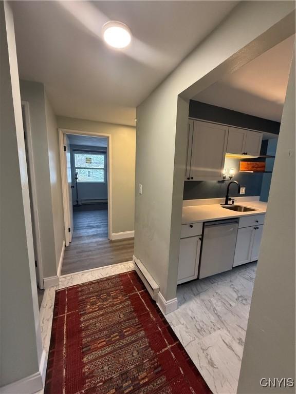 corridor featuring marble finish floor, baseboards, baseboard heating, and a sink