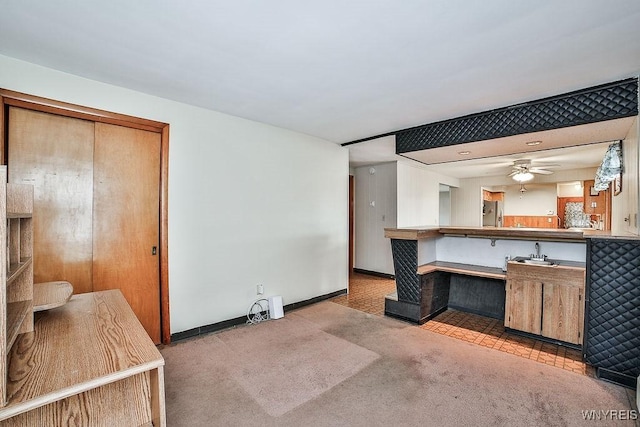 kitchen featuring a sink, carpet flooring, a ceiling fan, baseboards, and freestanding refrigerator