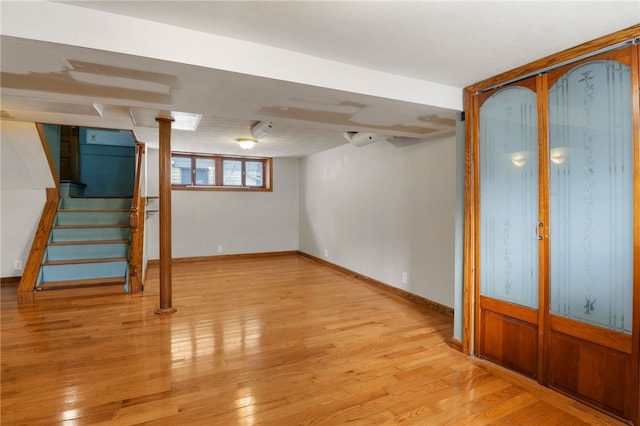 below grade area featuring baseboards, stairway, and light wood finished floors