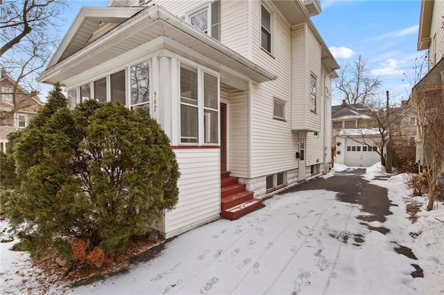 view of snowy exterior with a garage, entry steps, a sunroom, and an outdoor structure