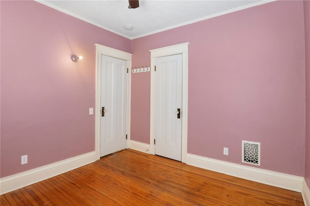 empty room with crown molding, wood-type flooring, visible vents, a ceiling fan, and baseboards