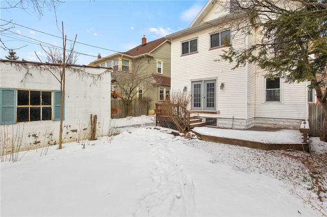 snow covered house featuring a deck, french doors, and fence