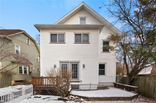 snow covered house with fence and a wooden deck