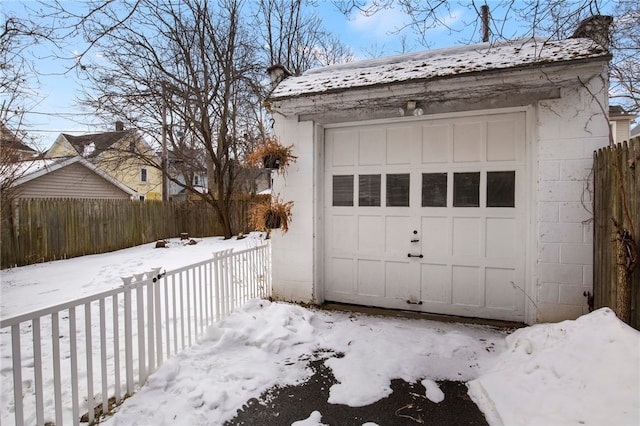 snow covered garage with fence and a detached garage