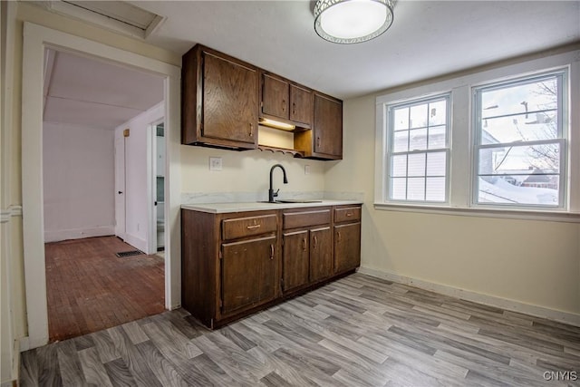 kitchen featuring visible vents, baseboards, light countertops, light wood-type flooring, and a sink