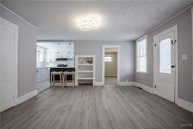 unfurnished living room with light wood-type flooring, baseboards, and ornamental molding