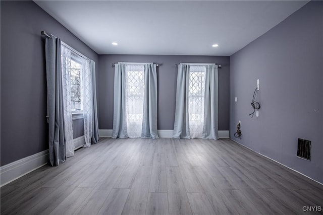 unfurnished room featuring baseboards, wood finished floors, visible vents, and a healthy amount of sunlight