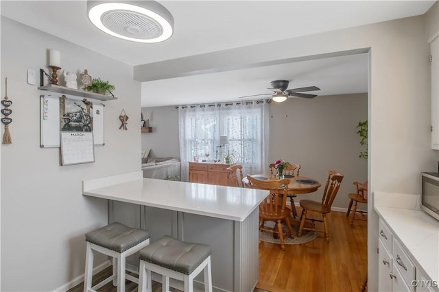 kitchen featuring a breakfast bar area, a peninsula, wood finished floors, white cabinets, and light countertops