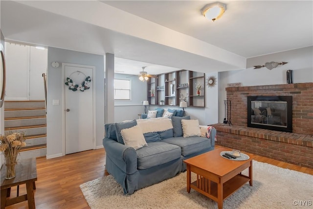 living area featuring light wood-style floors, a fireplace, stairway, and baseboards